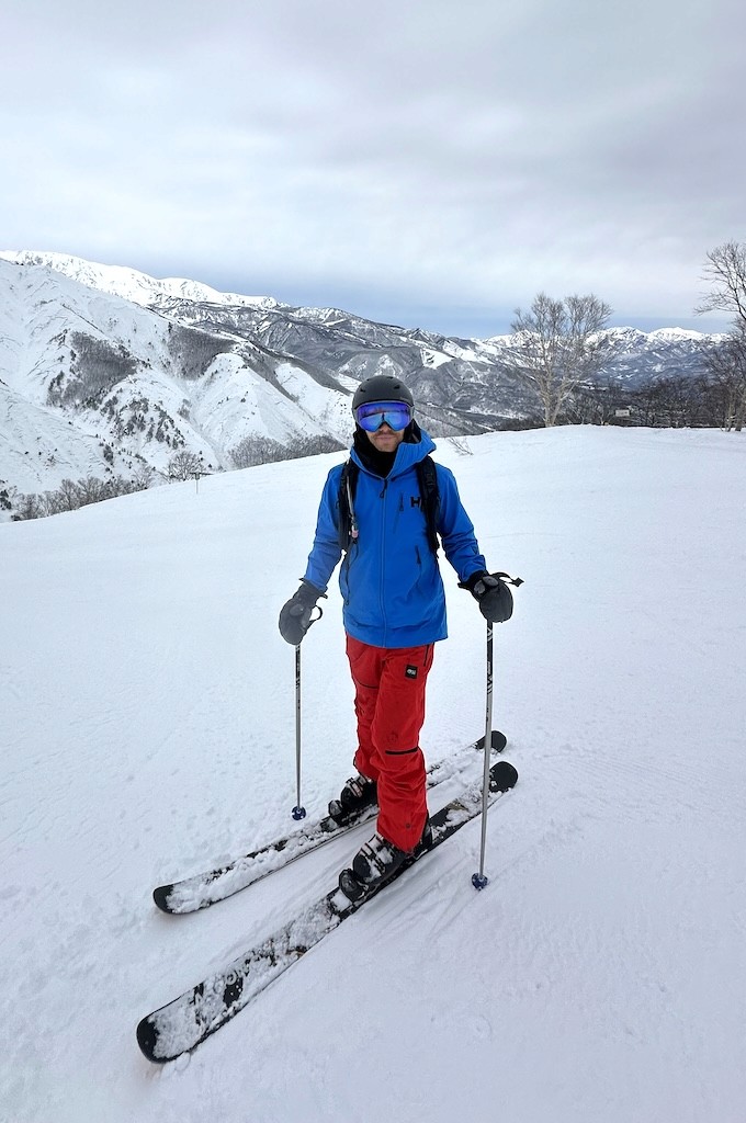 Paul skiing on a snowy mountain in blue and red gear.